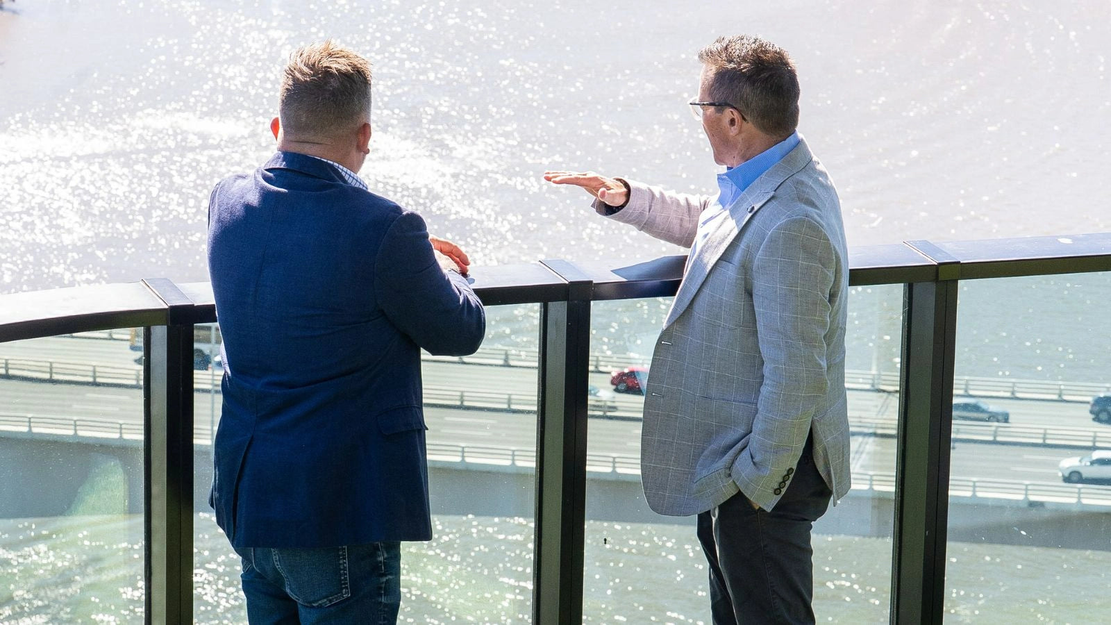 Back shot of Matt and Pepe while standing on a balcony overlooking a bridge and water