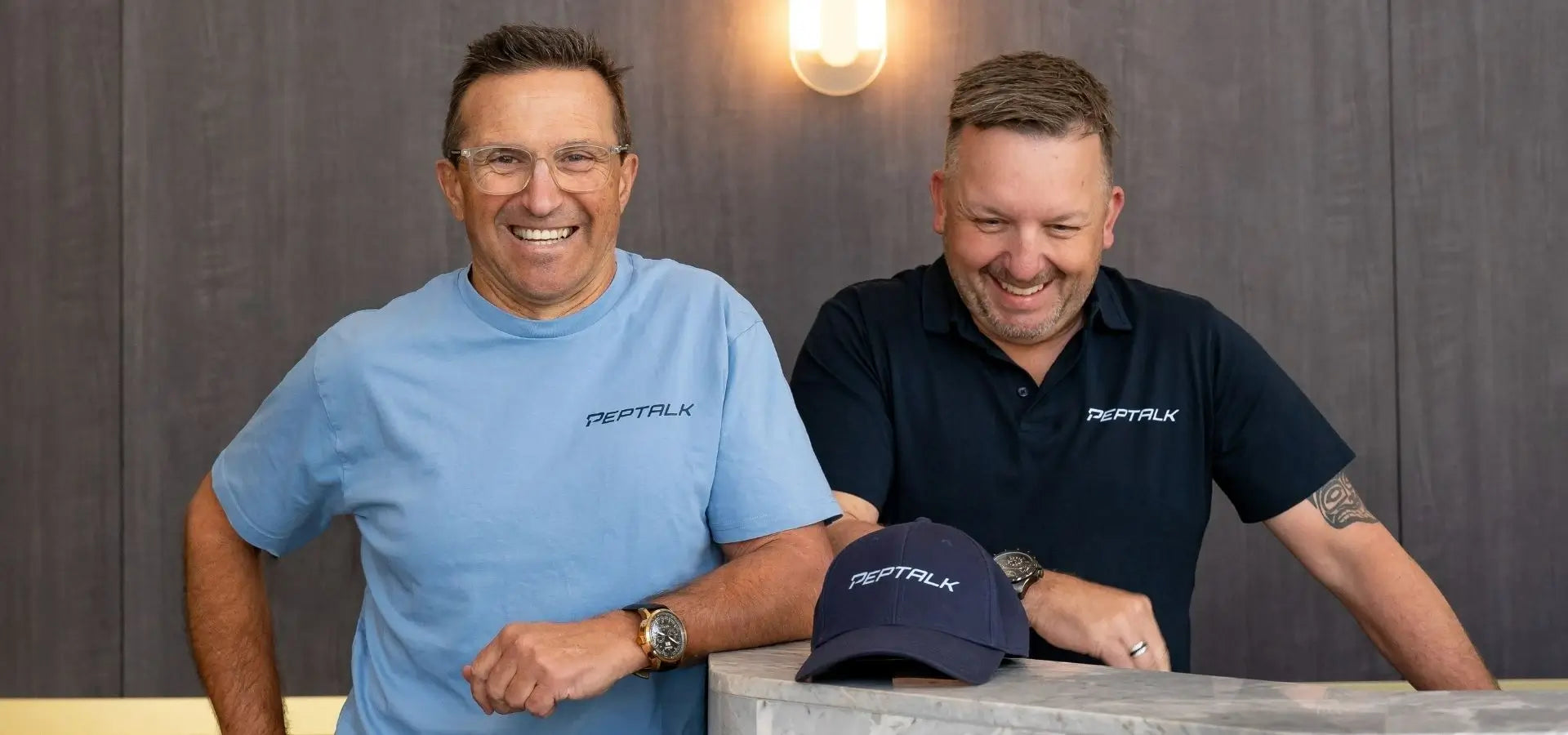 Photo of Pepe and Matt both smiling and wearing PepTalk shirts with a PepTalk cap in front of them