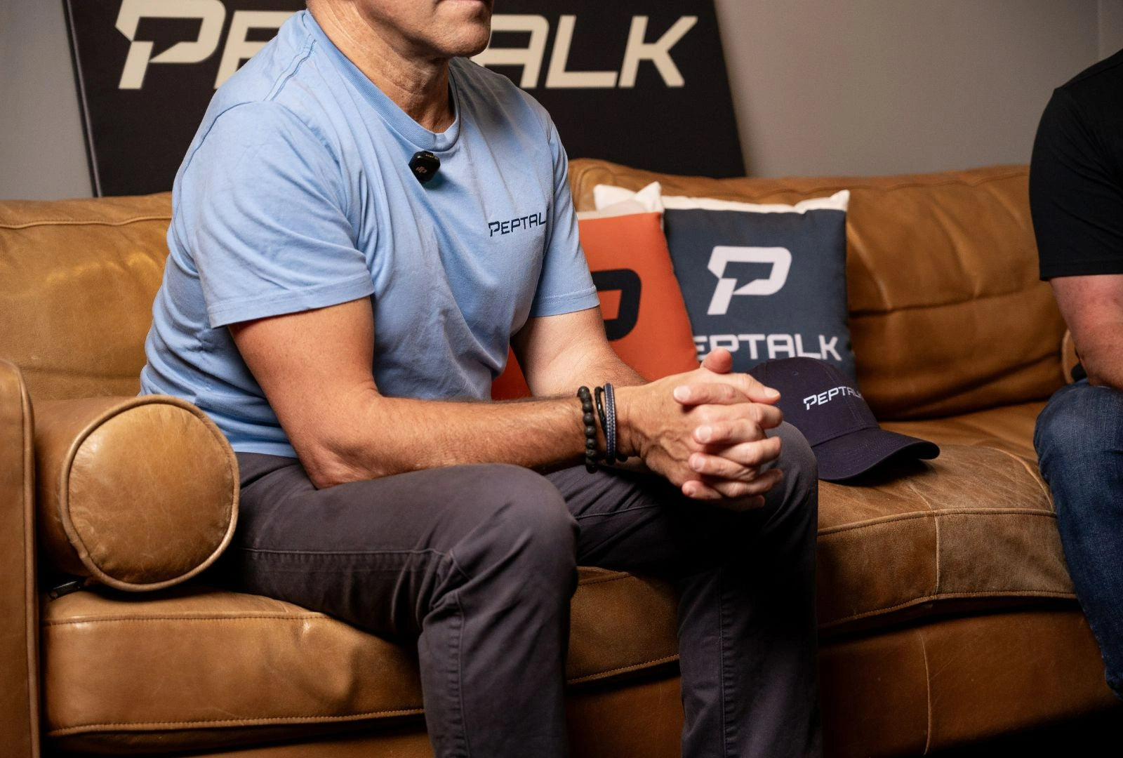Photo of Pepe wearing a PepTalk shirt while sitting on a leather couch and holding his hands together