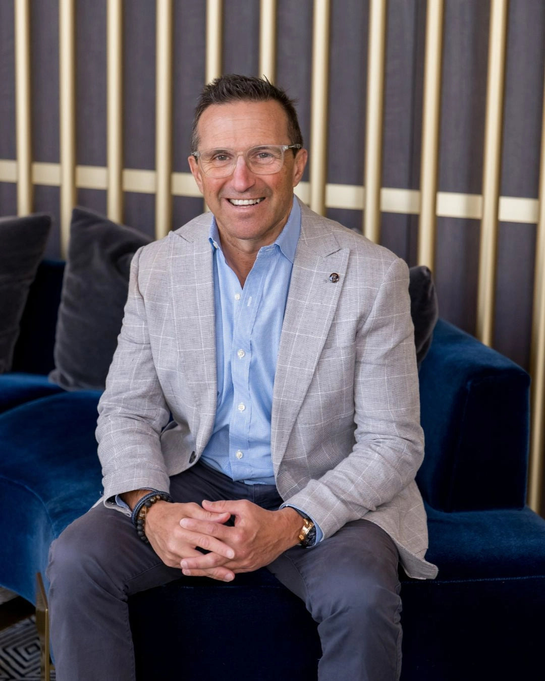Photo of Pepe Ianniello smiling and wearing a grey coat while sitting on a blue couch