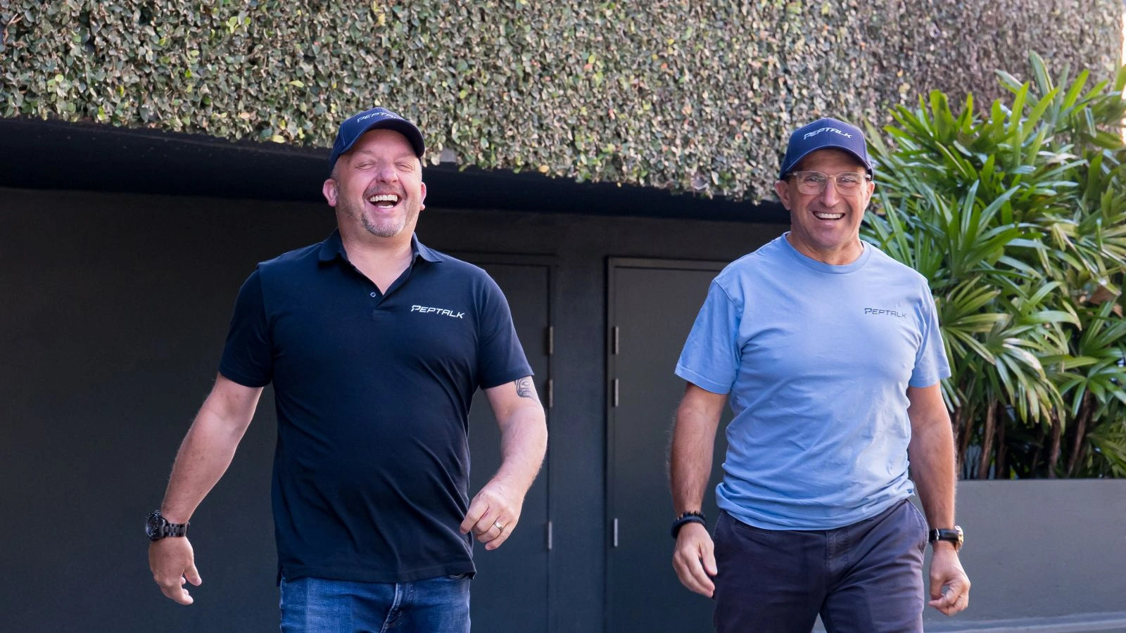 Photo of Pepe and Matt standing outdoors, Matt wearing a black shirt with PepTalk logo and Pepe in a blue shirt, against a green hedge background.
